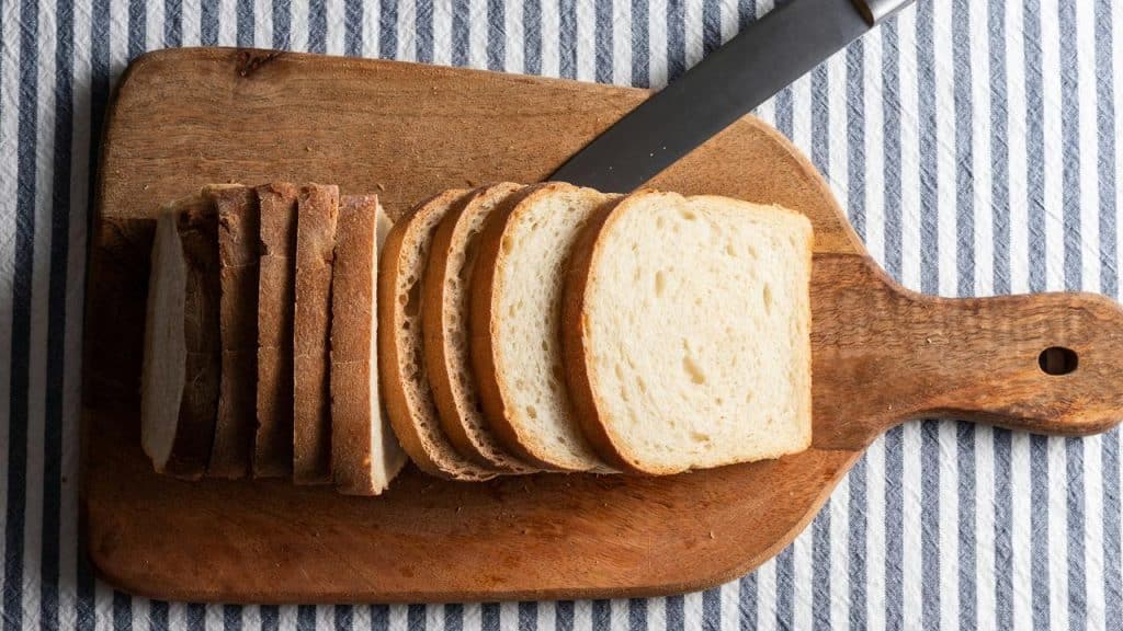 A loaf of sliced white bread arranged on a wooden cutting board with a bread knife resting beside it.