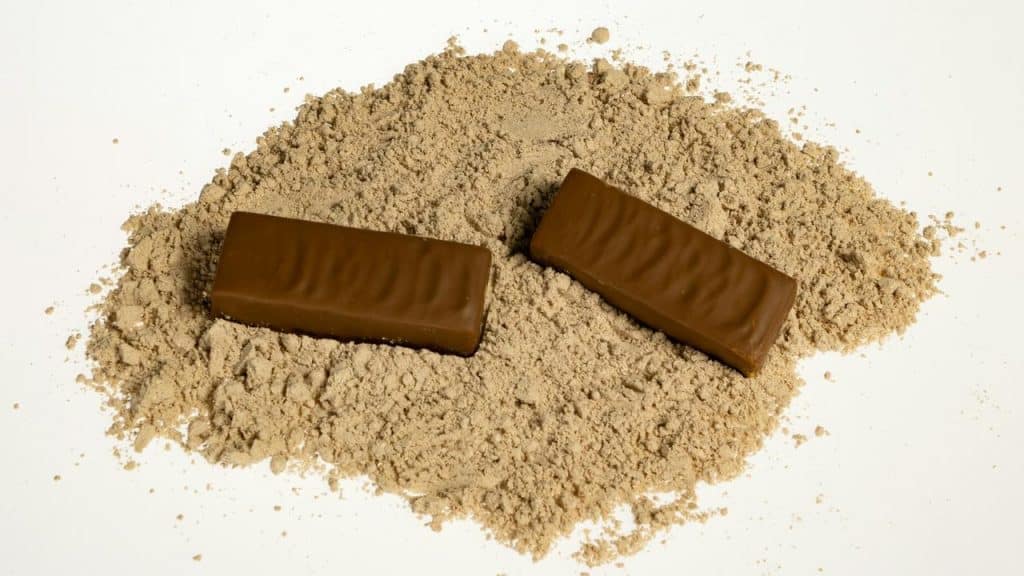 A pair of chocolate-covered bars on a mound of protein powder.