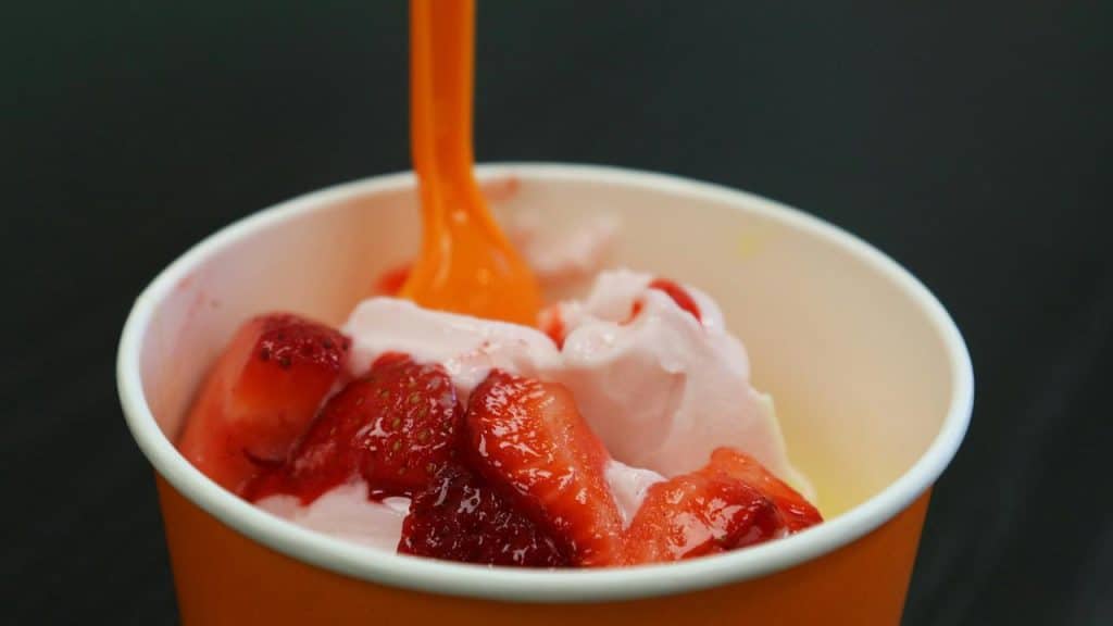 A cup of strawberry frozen yogurt topped with sliced strawberries and sauce.