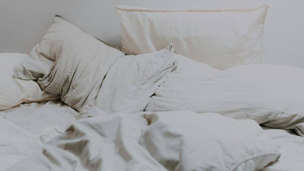 An unmade bed with crumpled white sheets and pillows.