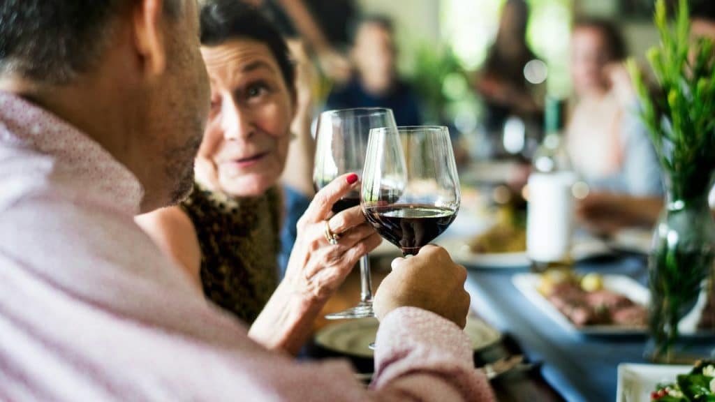 A pair toasting red wine glasses at a dinner table.