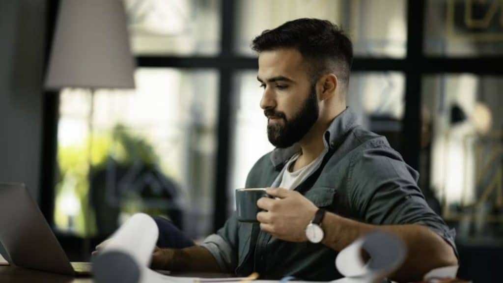 A man reviewing his expenses on a smartphone while drinking coffee