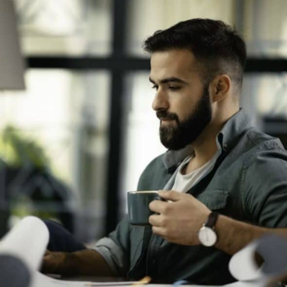 A man reviewing his expenses on a smartphone while drinking coffee