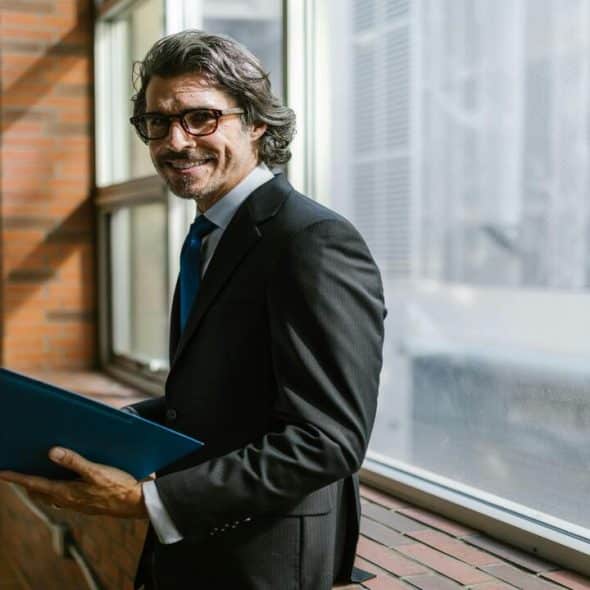 A man in a suit holding a blue folder.
