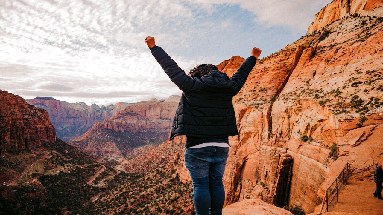 A man looking at a cliff with his hands in the air.