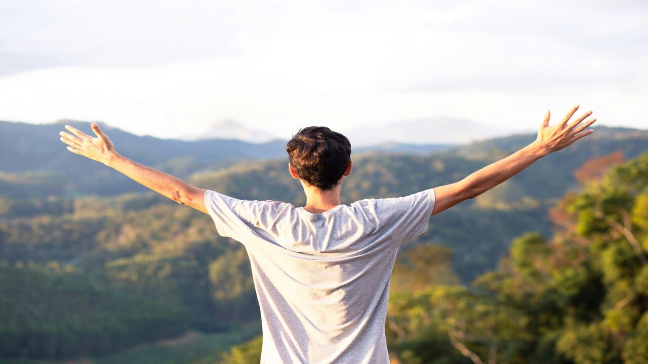 A man looking at the mountains with his hands in the air.