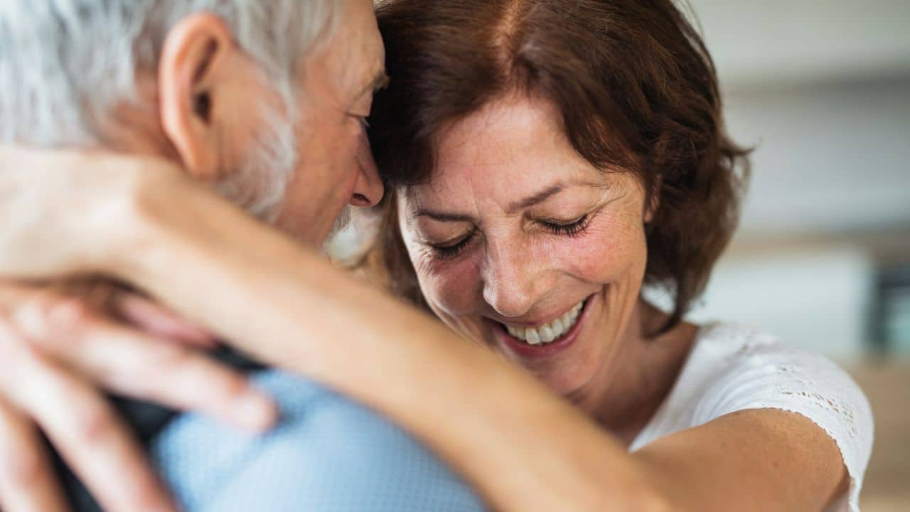 A happy woman with closed eyes hugs a man, smiling brightly.