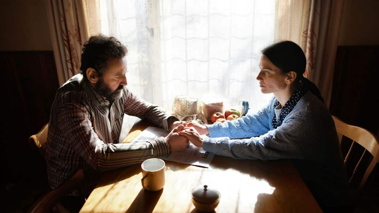 A man and woman hold hands across a table, looking serious.