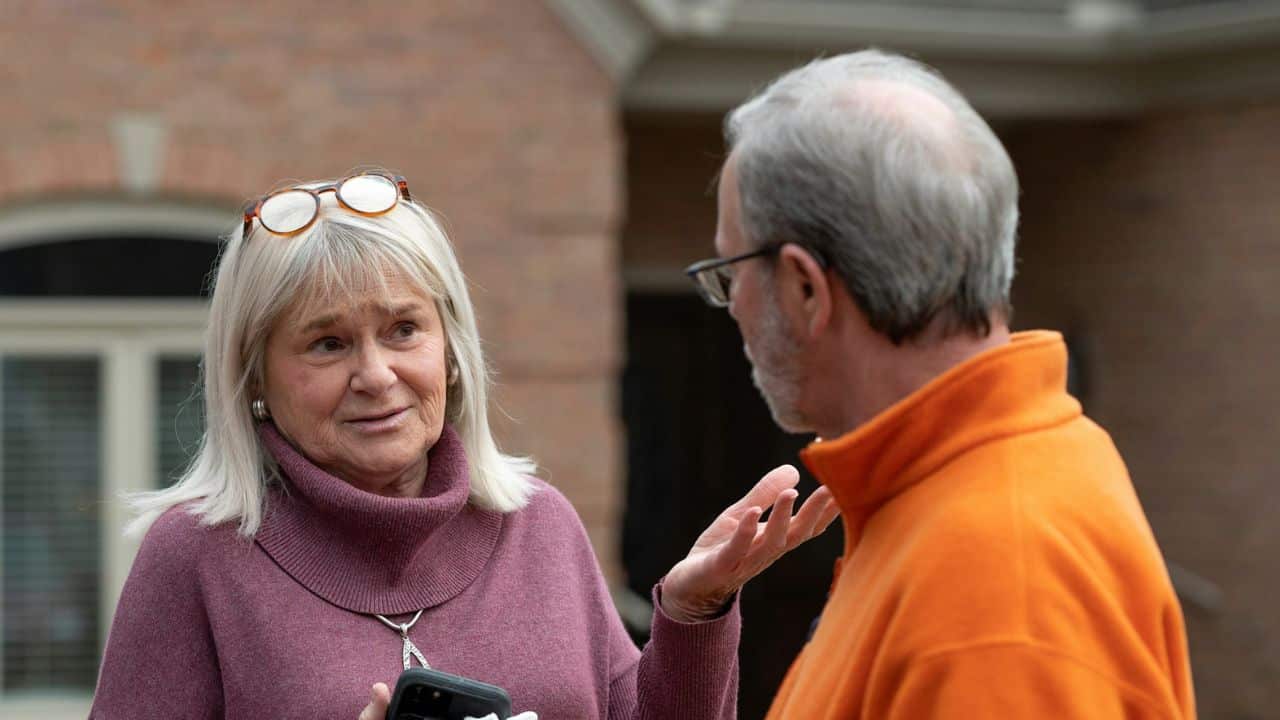 A woman with blonde hair gestures while talking to a man.