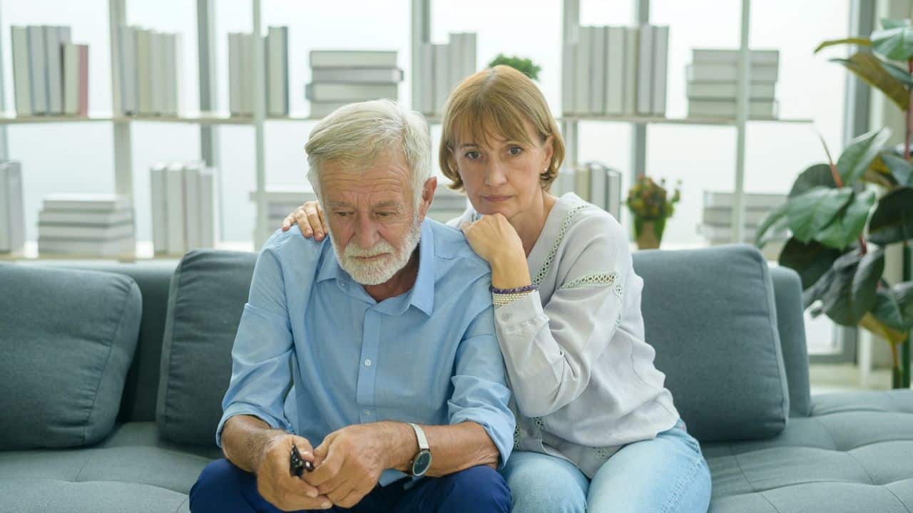 A concerned woman puts her hand on a sad man's shoulder.