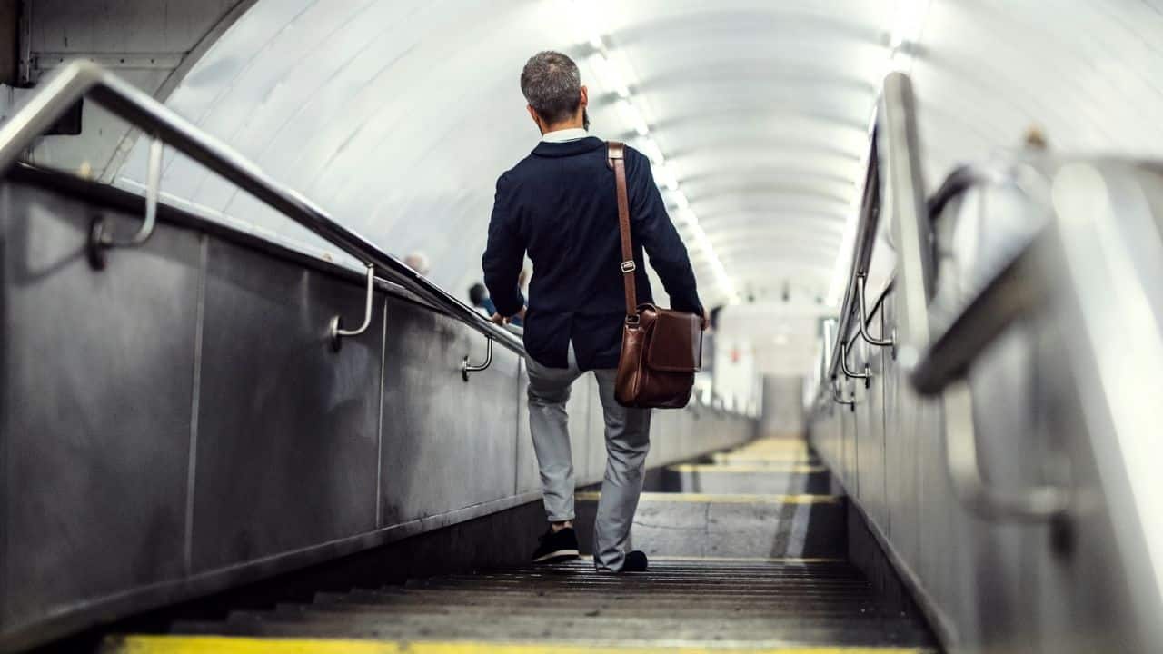 A man with a briefcase walks up an escalator in a subway station.