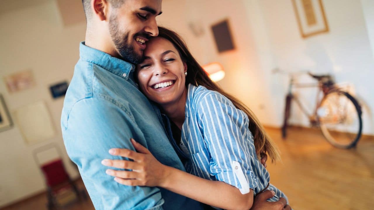 A laughing woman embraces a smiling man, holding onto him tightly.
