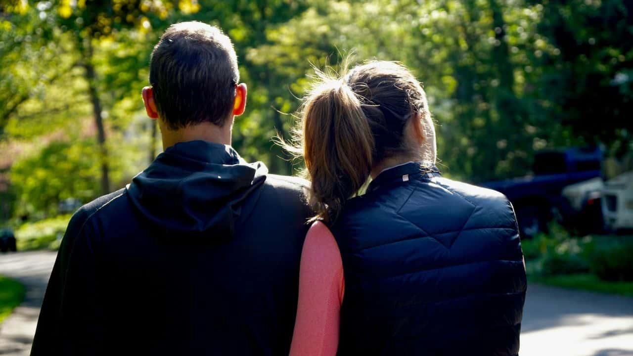 A man and woman, seen from behind, walk down a tree-lined path.