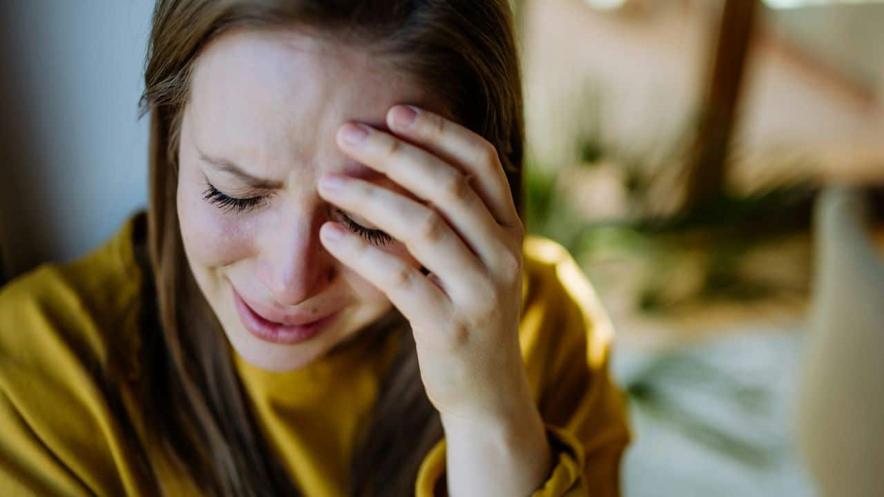 A crying woman with long hair covers her eyes with one hand.