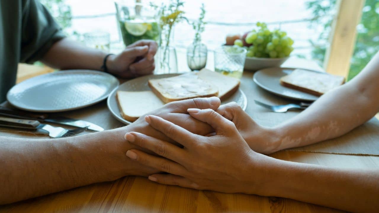 A man and a woman hold hands across a table set with breakfast items.
