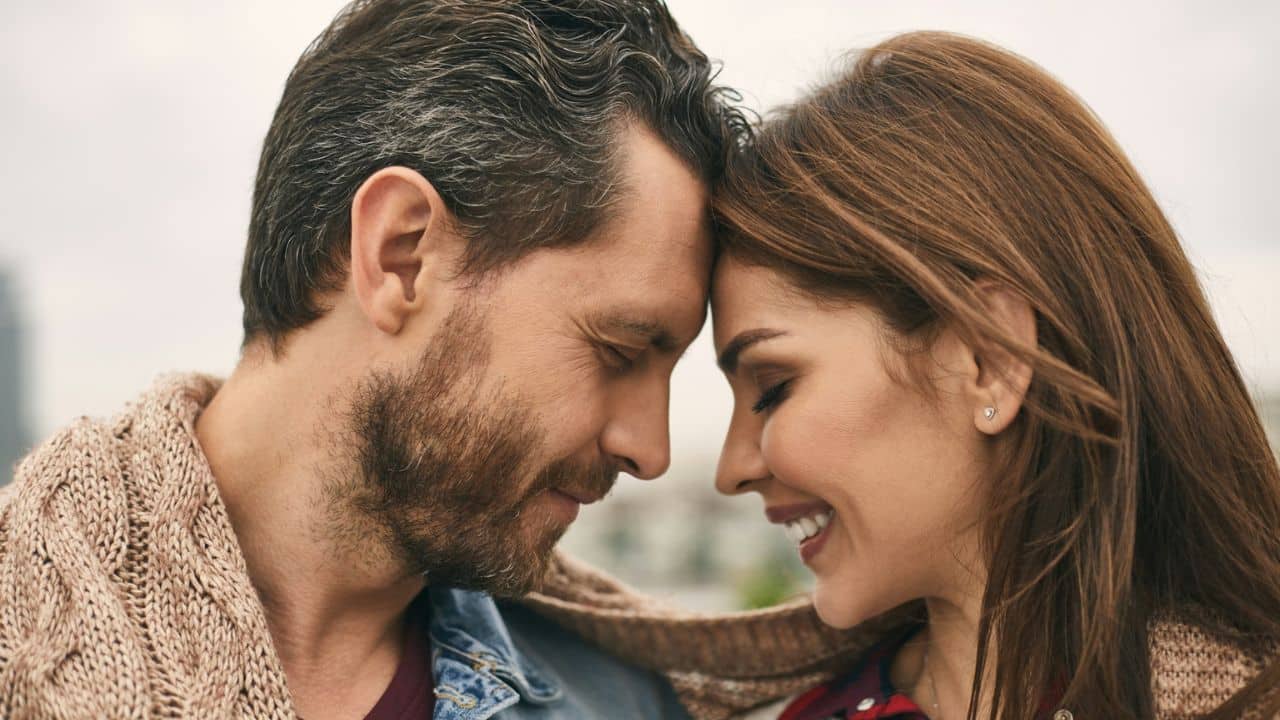 A man and a woman with closed eyes and smiling faces touch foreheads intimately.