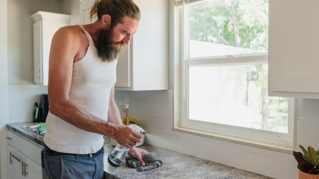 A man with a beard and hair tied back cleans a kitchen counter.