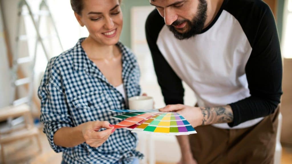 A smiling woman and a man look at color swatches, holding a mug and swatches respectively.