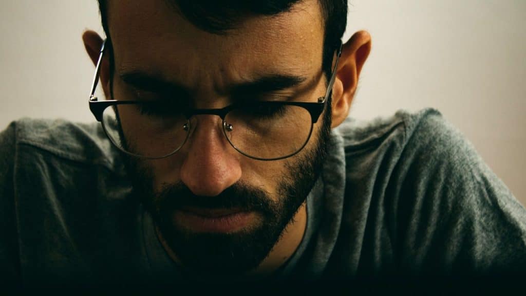 A man with glasses and a beard looks down intensely.