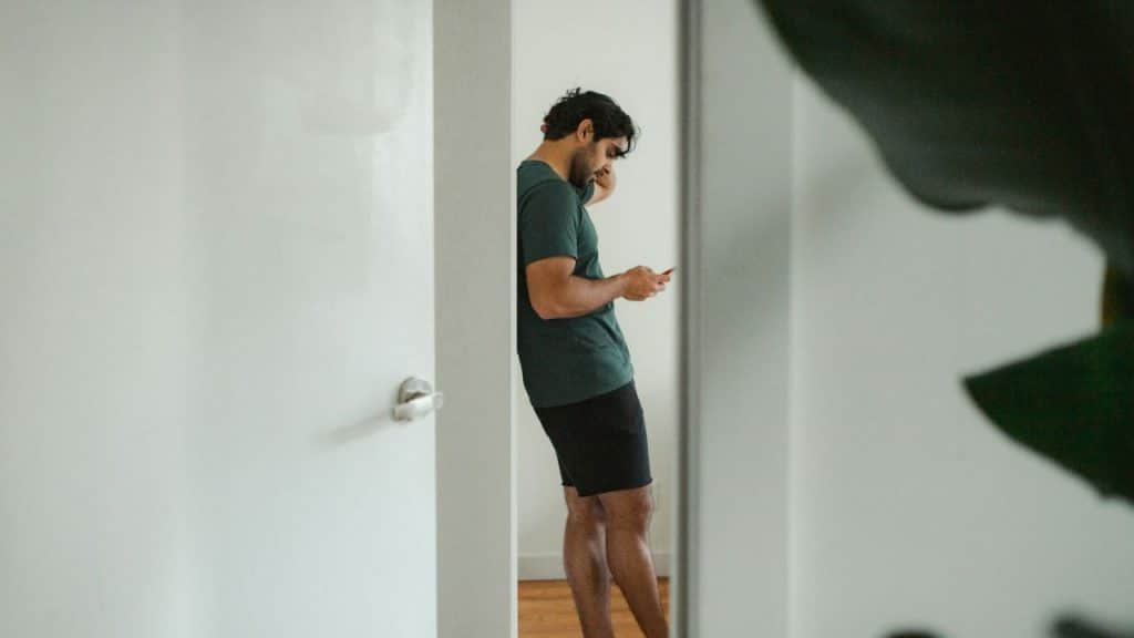 A man leans against a wall, looking at his phone.