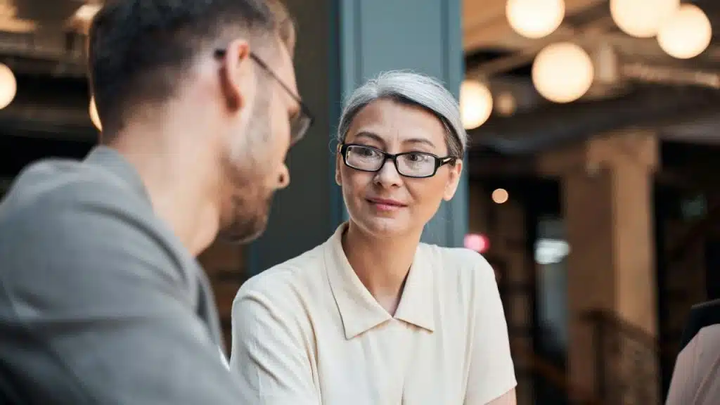 A grey-haired woman in glasses looks intently at a man.