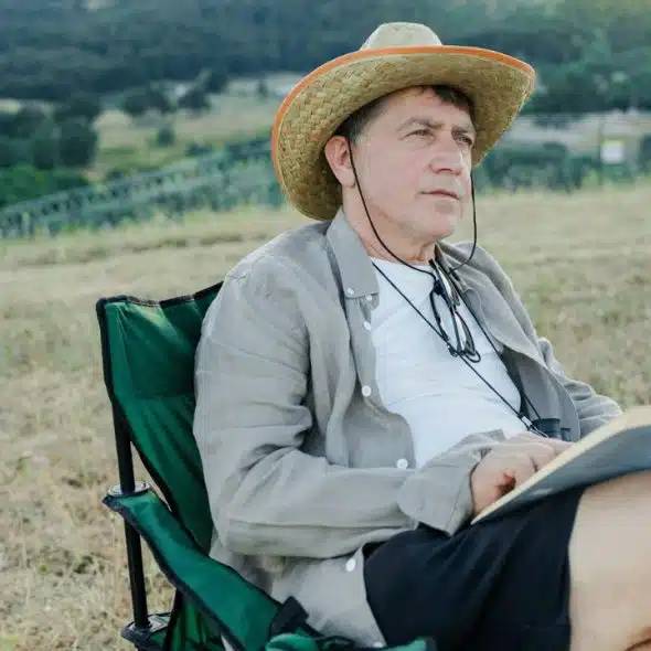 A man in a straw hat sits outdoors, reading a book.