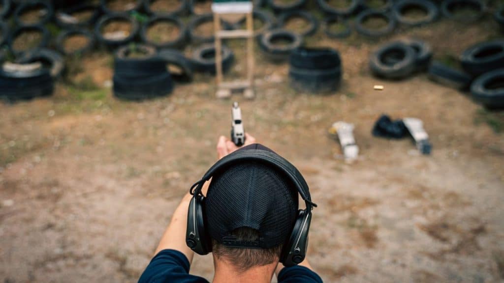 A person from a top-down view is firing a handgun at a target range, wearing ear protection.