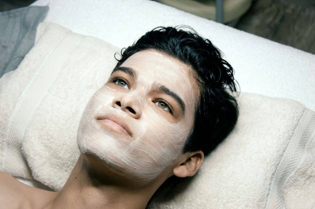 A man laying on bed with a cream on his face.
