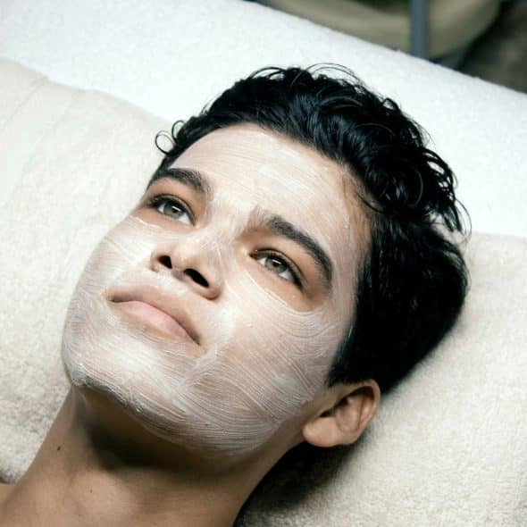 A man laying on bed with a cream on his face.