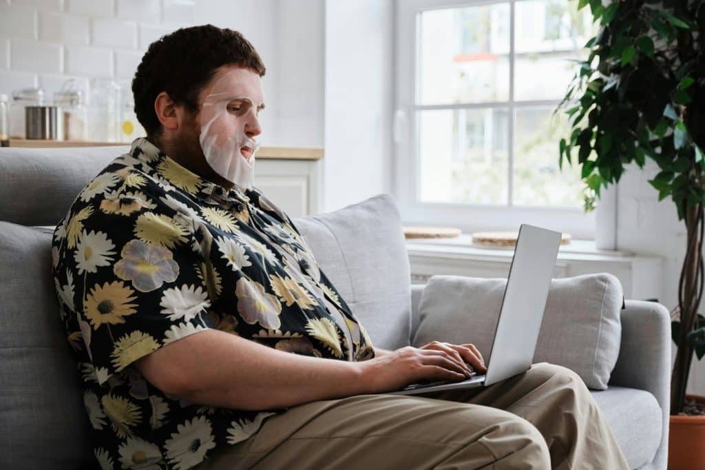 A man using a facial mask while watching on his laptop.
