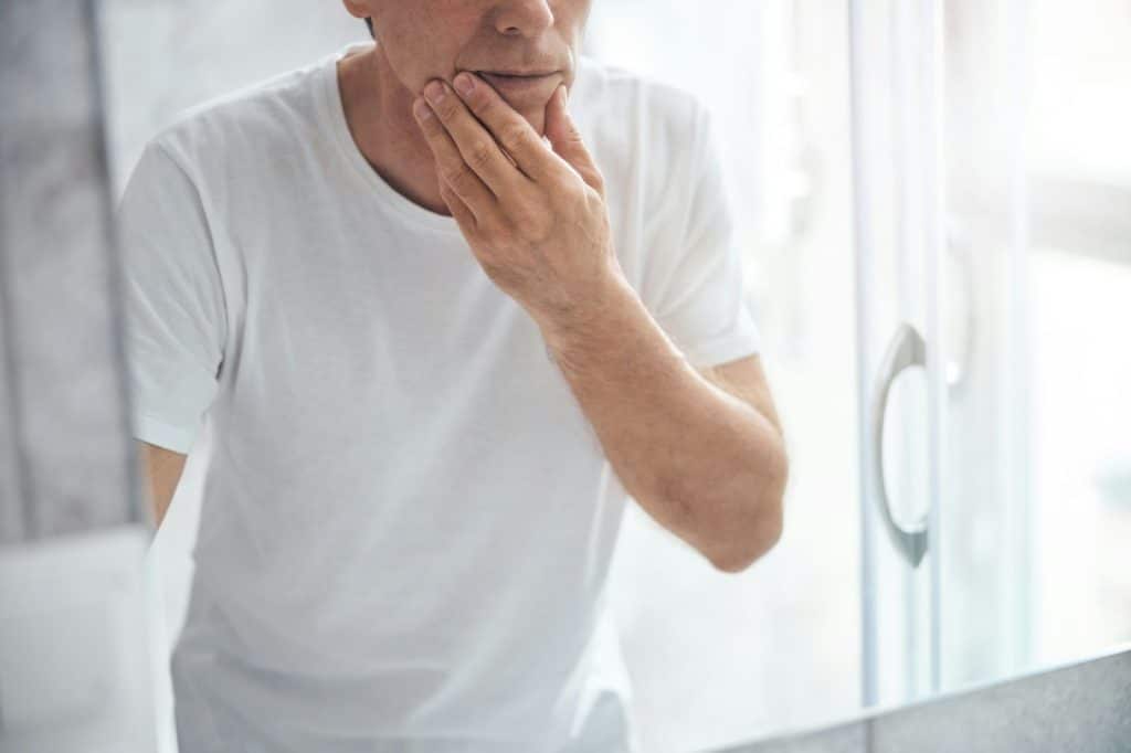 A man checking his face on the mirror.