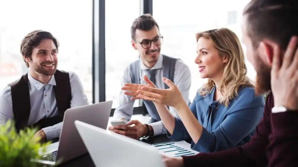Woman confidently presenting in a meeting while man looks on with pride