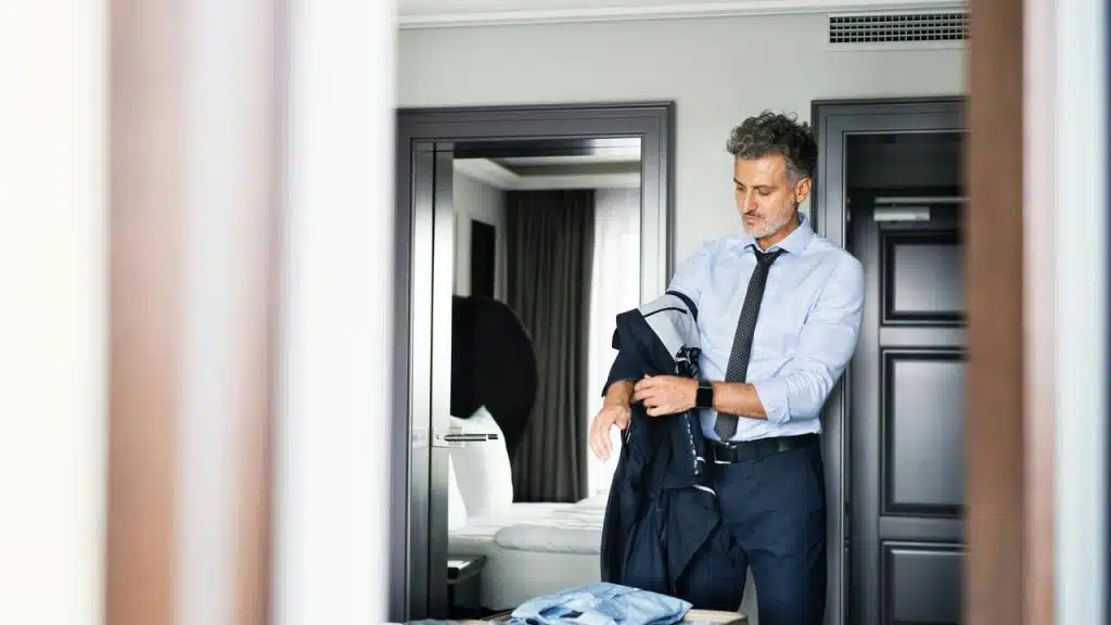 A man putting on his suit jacket in a hotel room.