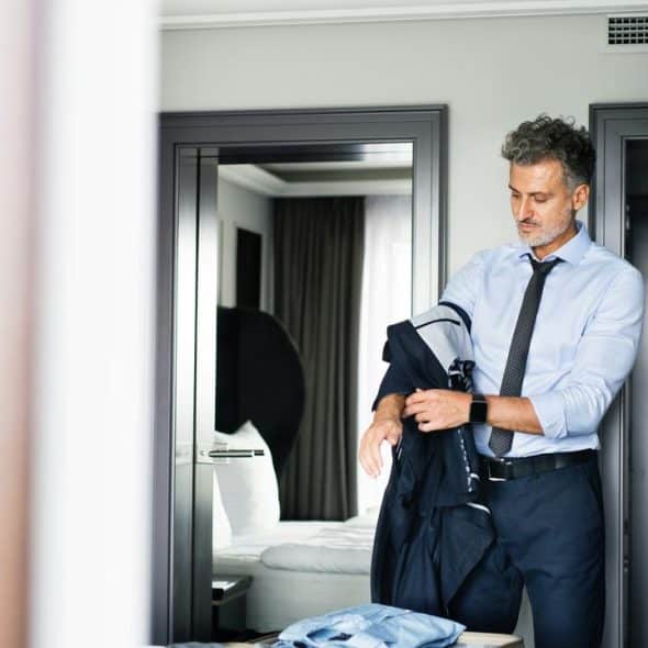 A man putting on his suit jacket in a hotel room.