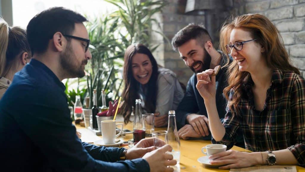 A group of friends laughing over coffee as one holds a cookie.