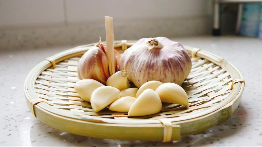 A bamboo tray holding garlic bulbs and peeled cloves.