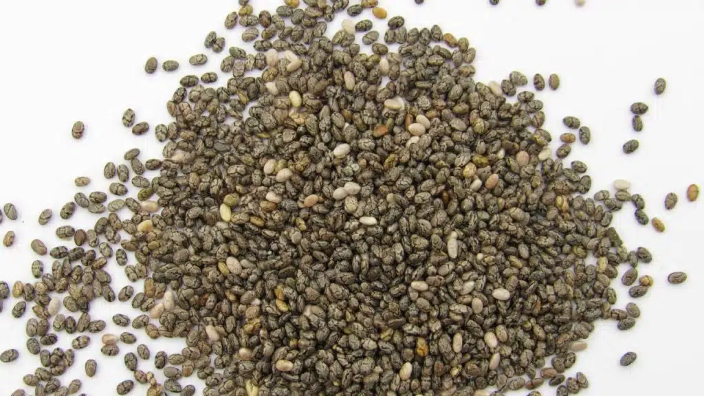 A pile of speckled chia seeds scattered on a white surface.