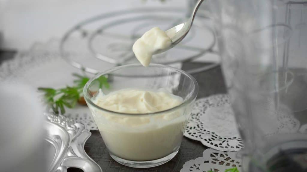 A spoon lifting creamy yogurt above a glass bowl of yogurt.