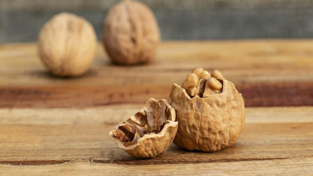 A cracked walnut on a wooden board with two whole walnuts blurred in the background.