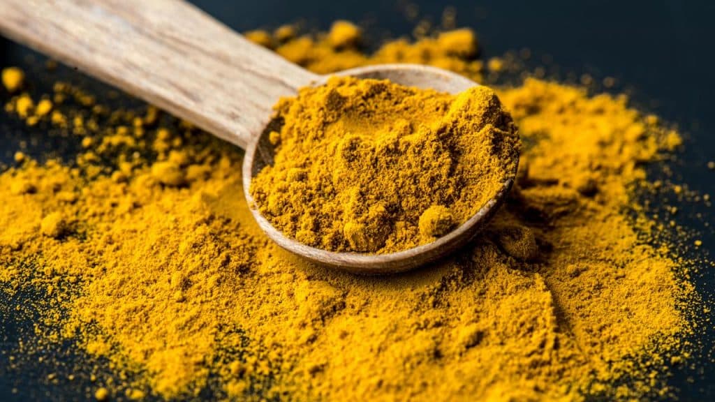 A wooden spoon heaped with golden turmeric powder on a dark surface.