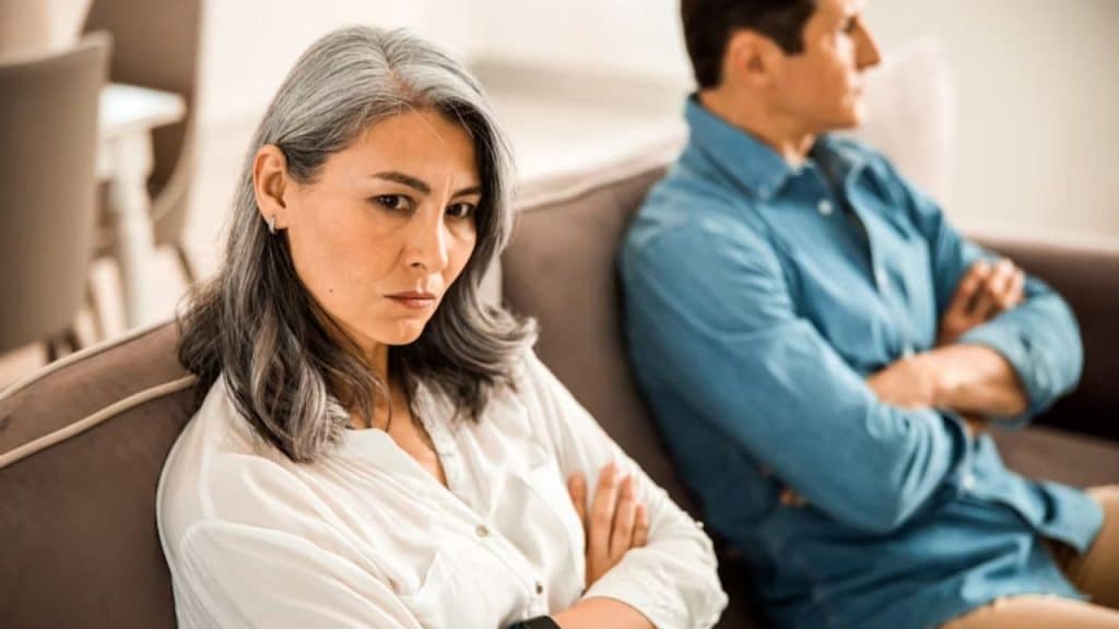 Emotionally distant couple sitting far apart in a shared space.ALT Text: Emotionally distant couple sitting far apart in a shared space.