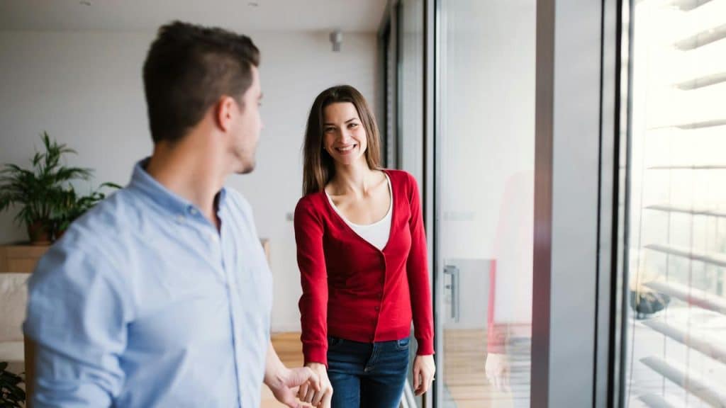 A smiling woman holding a man’s hand as they walk through glass doors.