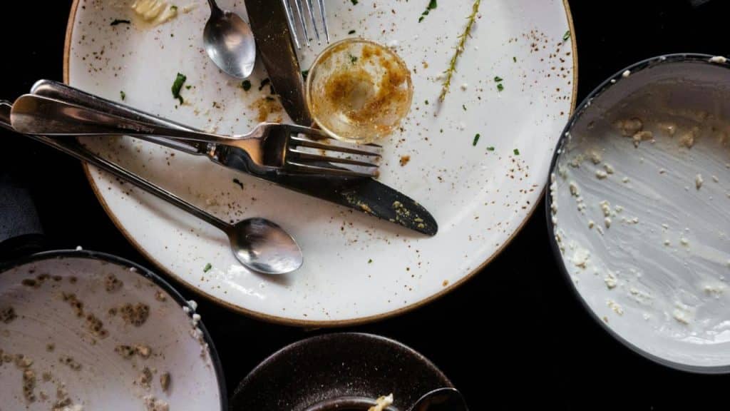 A set of empty, crumb-speckled plates with scattered forks, spoons, and a knife on a dark surface.