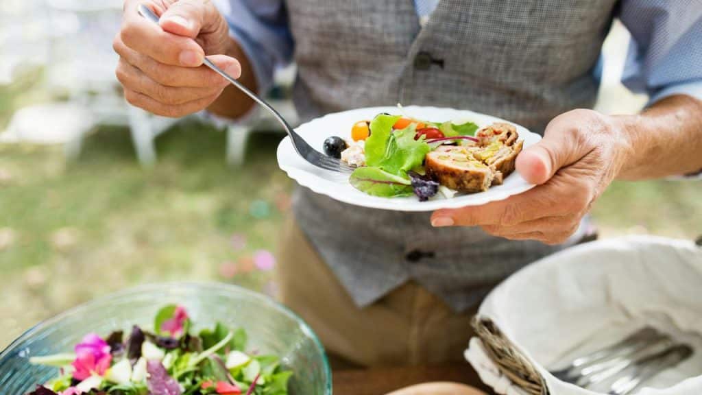 A person holding a plate of salad and roulade with a fork.