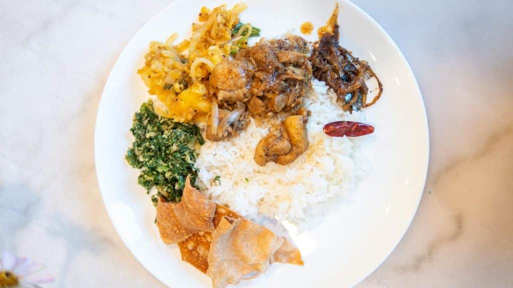A plate of rice topped with chicken curry, greens, spiced vegetables, and crispy papadum.
