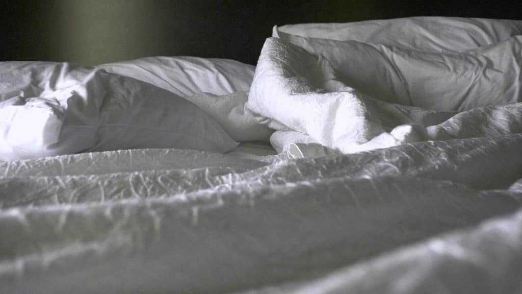 An unmade bed with rumpled white sheets and pillows.