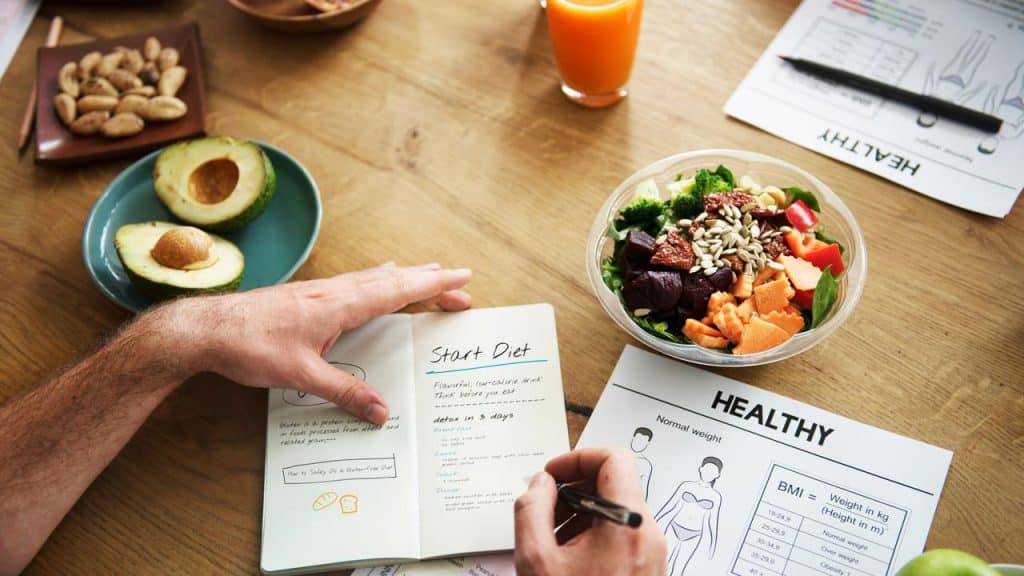 A person writing a diet plan beside a salad bowl.