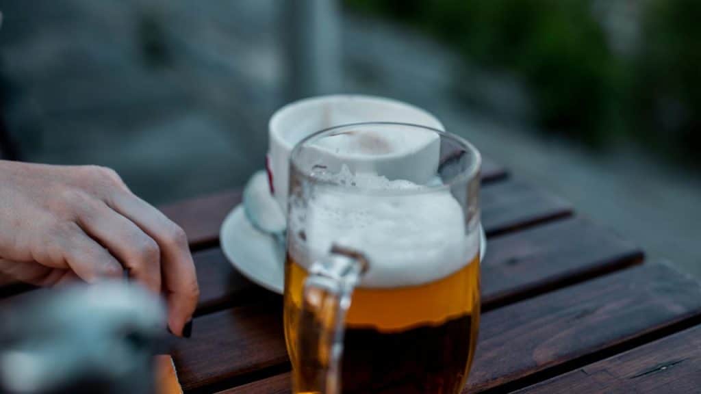 A frothy beer mug beside a coffee cup on a wooden table.