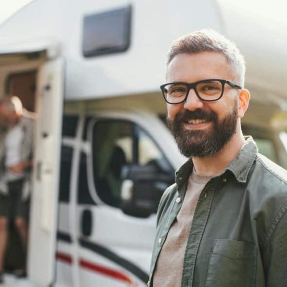 A smiling bearded man with glasses in front of an RV.