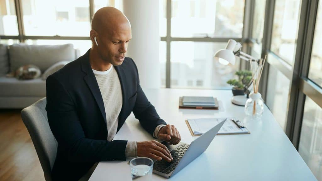 A man in earbuds typing on a laptop at a desk.